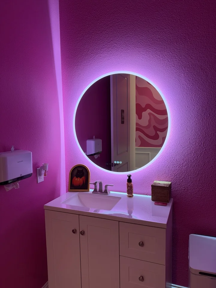 Bright pink washroom with a round illuminated mirror at YA Studio